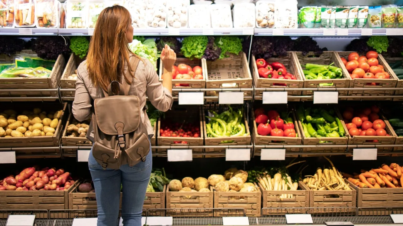 8c1d933c-good-looking-woman-standing-front-vegetable-shelves-choosing-what-buy Νέες μειώσεις τιμών σε σούπερ μάρκετ